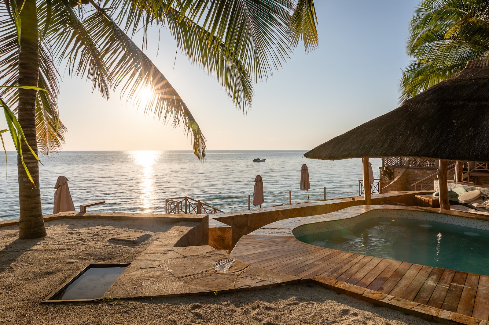 Hammock strung between wooden posts overlooks turquoise lagoon waters at Tulia Zanzibar, with palm trees, manicured lawn, and pool edge in foreground.
