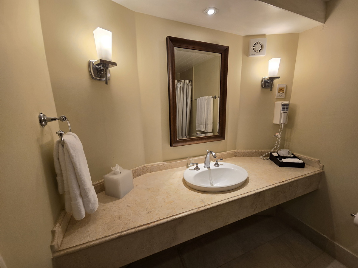Bathroom vanity with round white sink, framed mirror, sconces, and folded towels at Turtle Beach, Barbados.