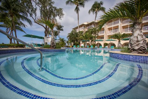 Curved swimming pool with blue tile design at Turtle Beach Resort, framed by palm trees and multi-story beige buildings under partly cloudy sky.