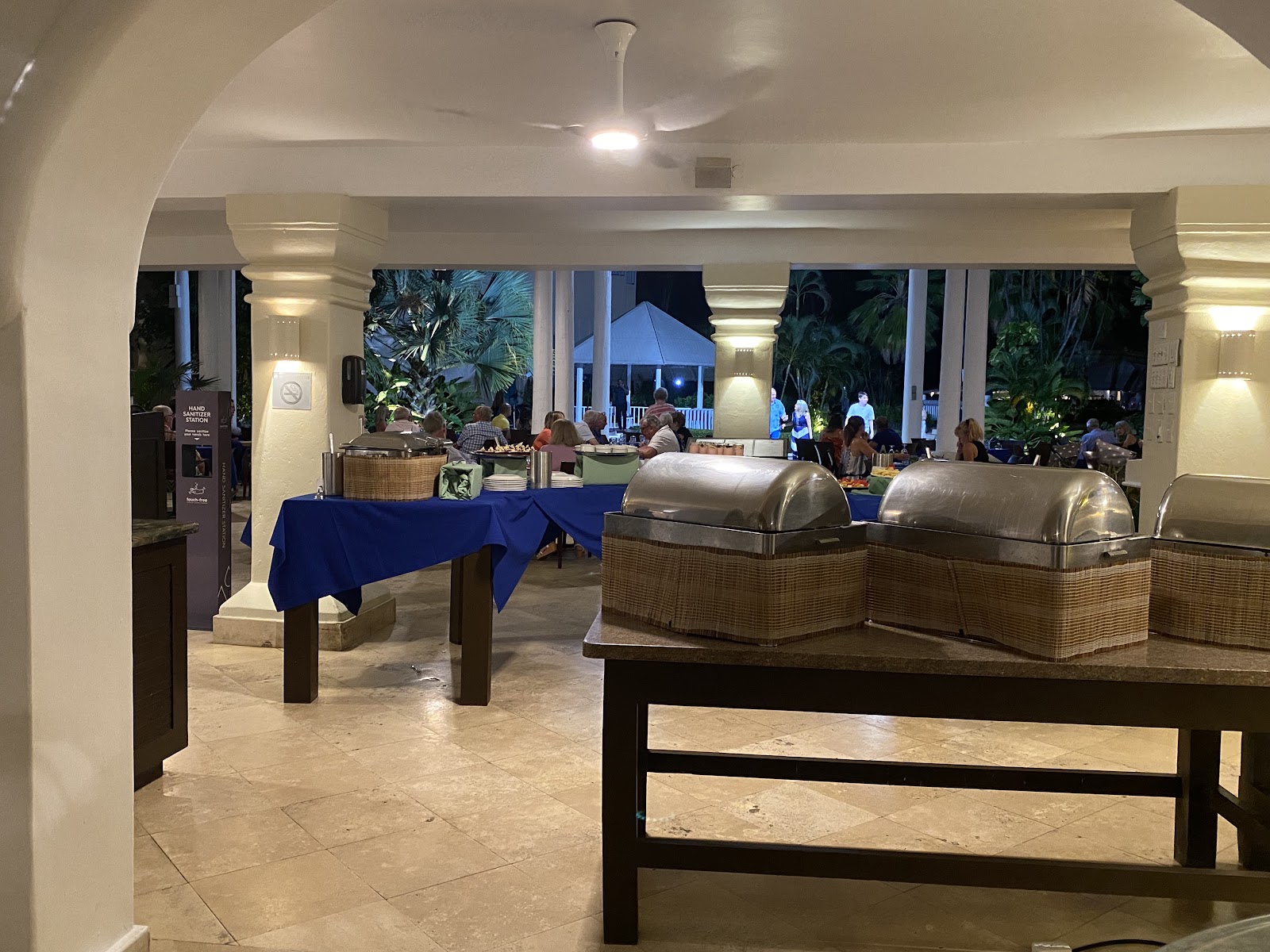 Evening buffet service at Turtle Beach Resort with stainless steel warming stations, blue-draped tables, and guests dining on an outdoor terrace beyond.