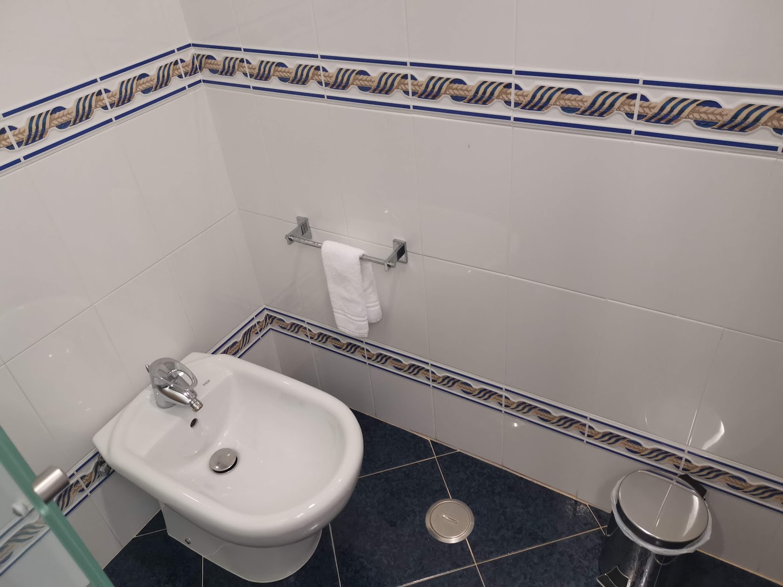 Bathroom with white round sink, toilet, and towel rack with white towel, decorated with blue and tan patterned tile trim.