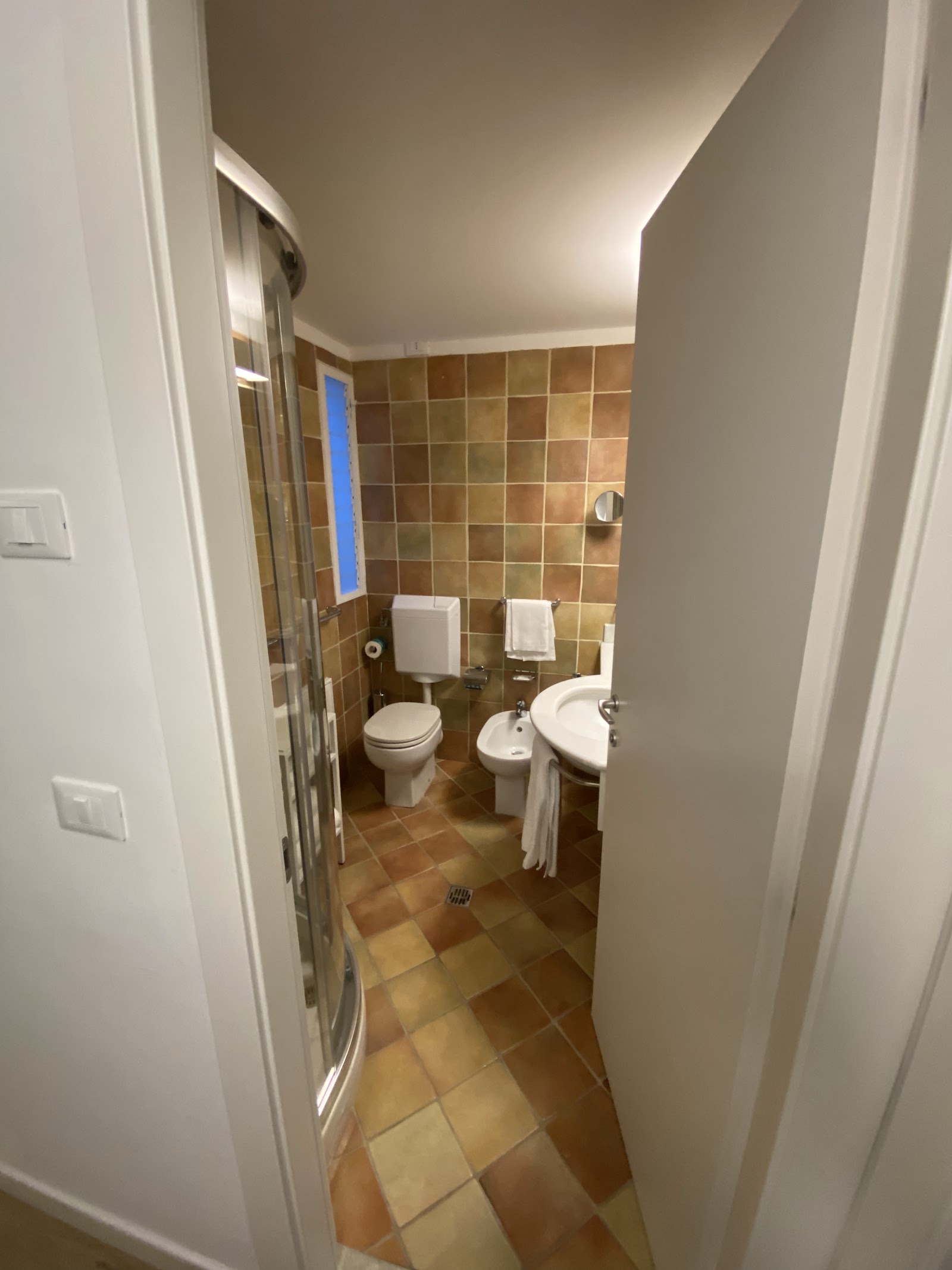 Resort bathroom with brown tile walls, glass shower enclosure on left, toilet, bidet, and sink with white towels.