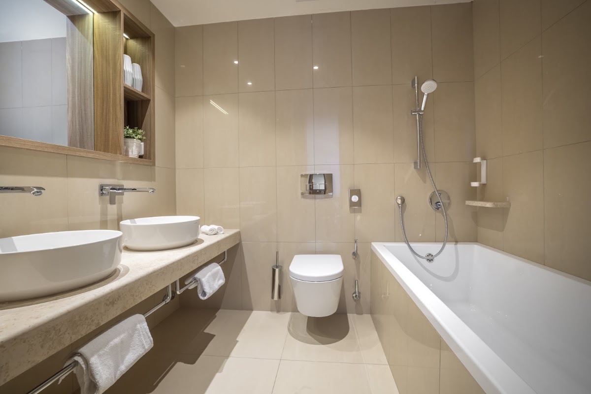 Modern resort bathroom with dual vessel sinks, soaking tub, walk-in shower, and beige tile throughout at Valamar Bellevue Resort.