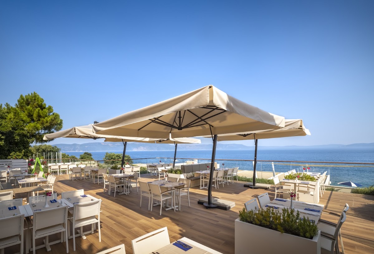 Beige umbrellas shade dining tables on a wooden deck overlooking the Adriatic Sea at Valamar Bellevue Resort.