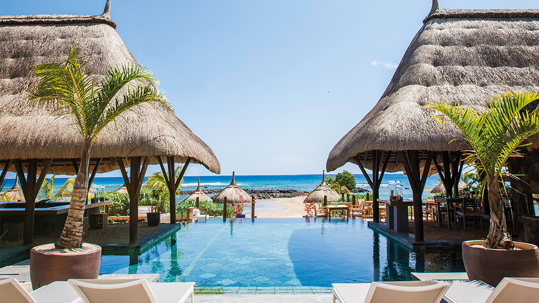 Thatched-roof bungalows frame a reflective pool leading to the ocean beach at Veranda Pointe aux Biches in Mauritius.