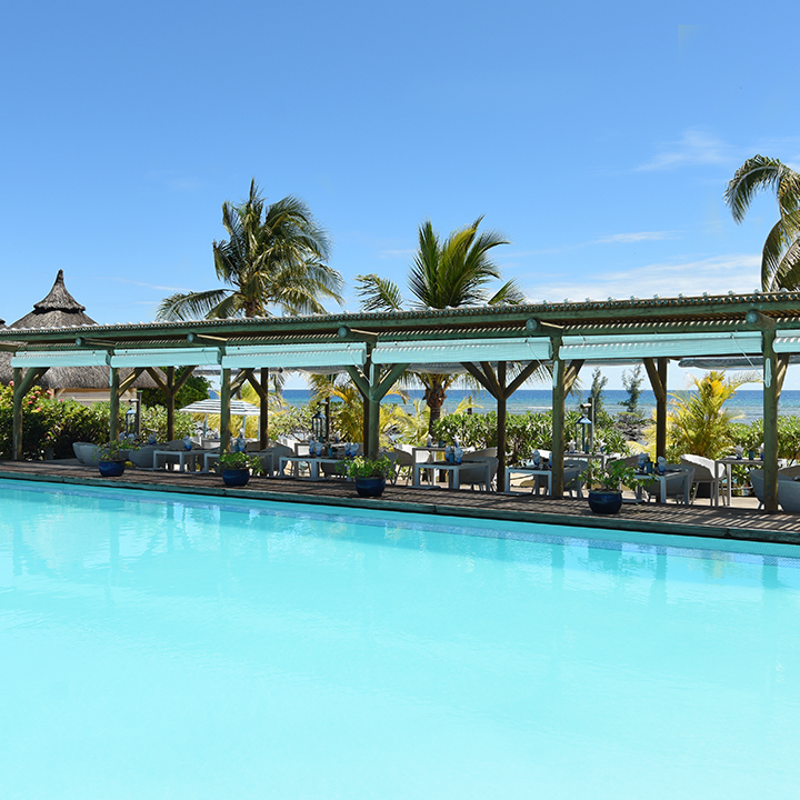 Turquoise pool with covered lounge area, palm trees, and ocean view at Veranda Pointe aux Biches in Mauritius.