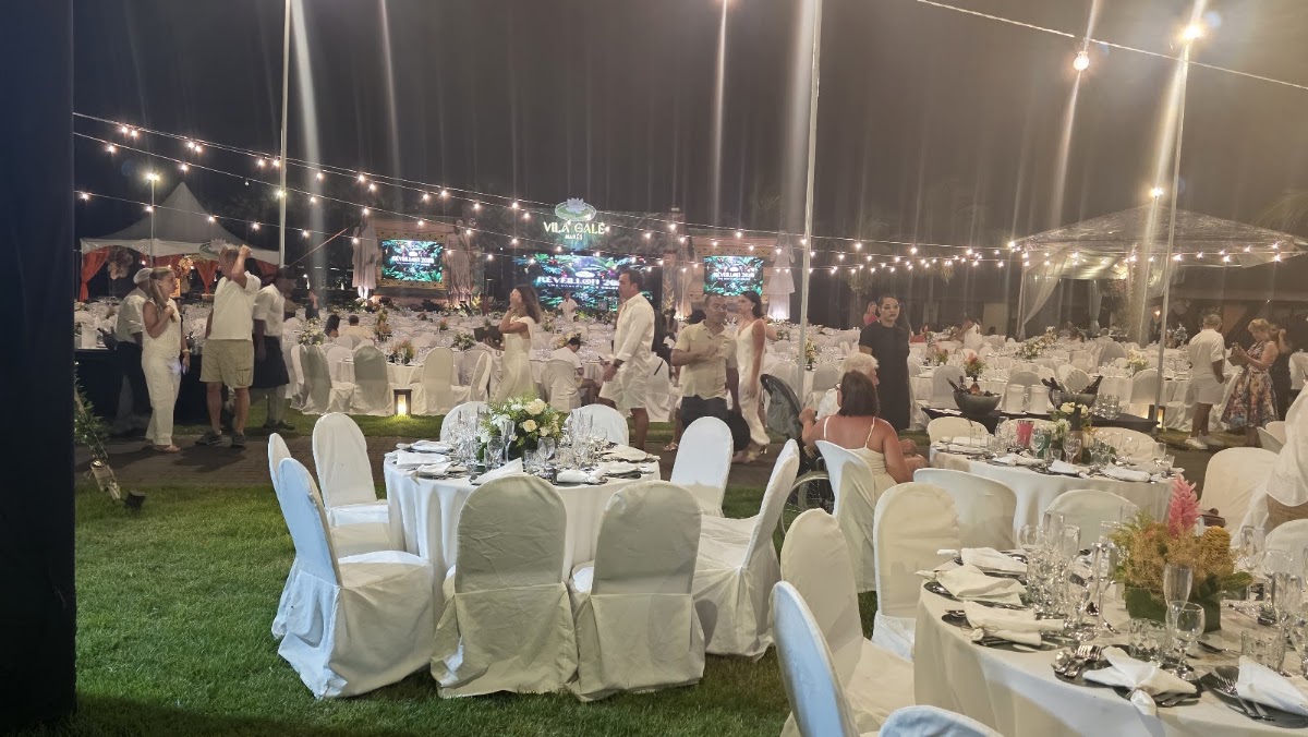 Nighttime outdoor gala dinner at Vila Galé Marés with white-draped tables on grass, string lights overhead, and guests mingling under illuminated tent structures.