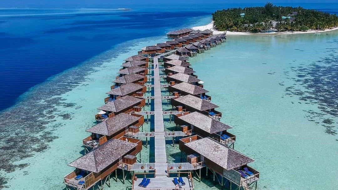 Aerial view of Vilamendhoo Island Resort & Spa's overwater bungalows arranged in symmetrical rows along a wooden jetty in turquoise lagoon waters.