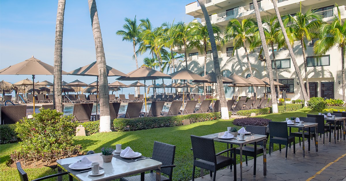 Beach area with blue and white loungers beneath thatched palapas, manicured lawn with topiary archway, and ocean view at Villa del Palmar.