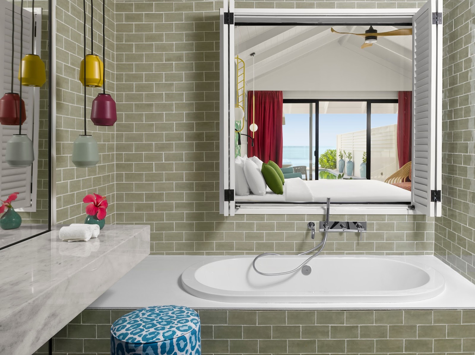 Modern bathroom with green subway tile walls, white soaking tub, and large mirror reflecting bedroom with ocean view at Villa Park, Maldives.