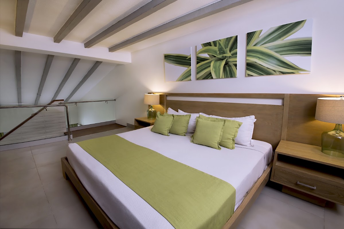 Upstairs bedroom with wooden bed, green and white bedding, exposed beam ceiling, and botanical wall art above nightstands.
