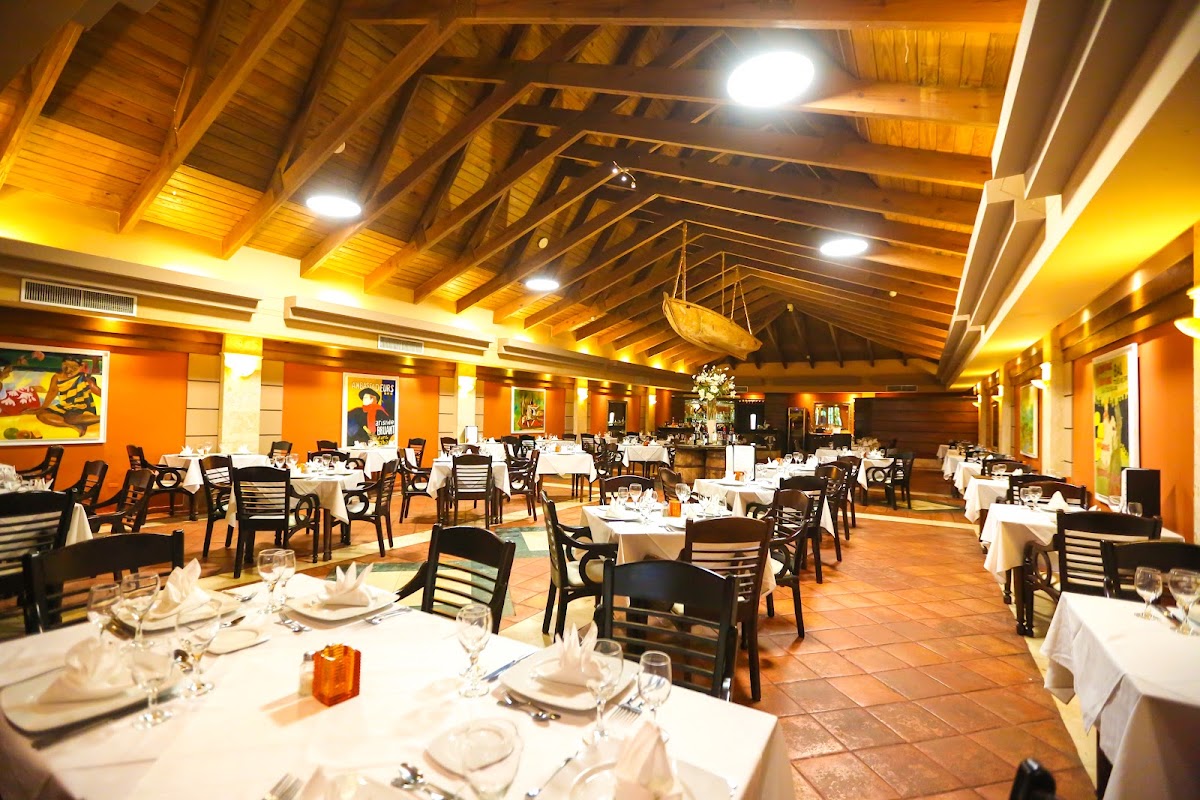 Dining room with white-clothed tables, black chairs, orange walls, and wooden ceiling with warm lighting at Vista Sol Punta Cana Beach Resort & Spa.