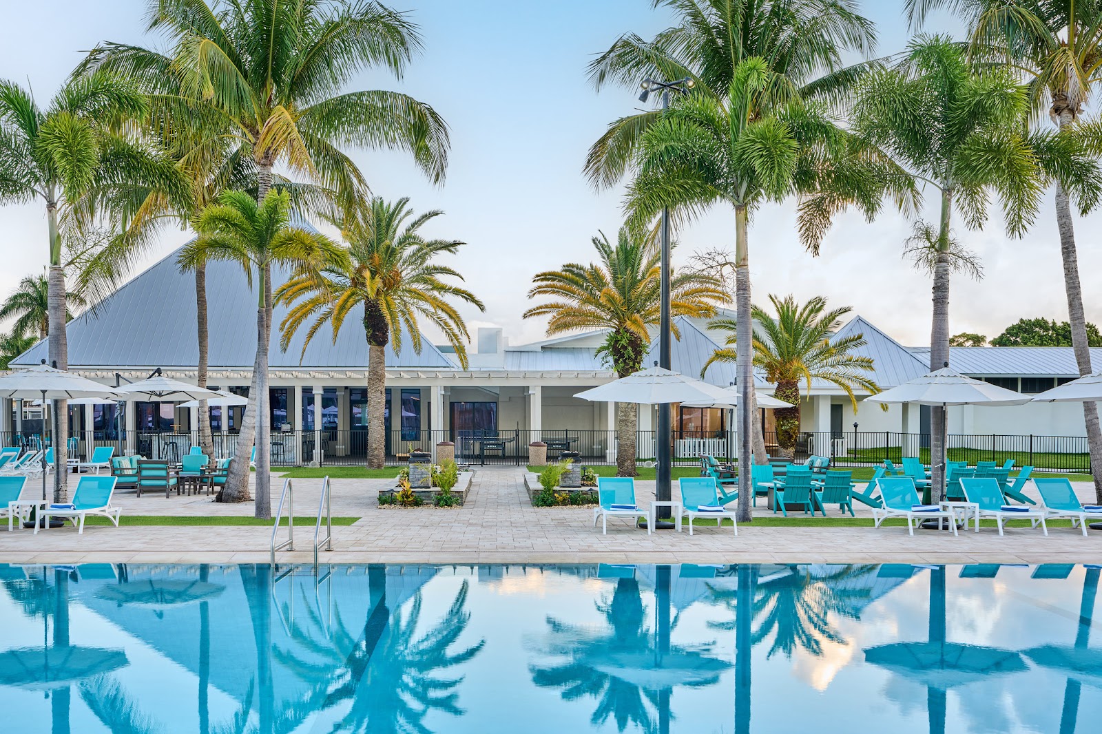 Blue pool with turquoise loungers, white umbrellas, and palm trees lining the voco Sandpiper All-Inclusive Resort's waterfront terrace and white buildings.