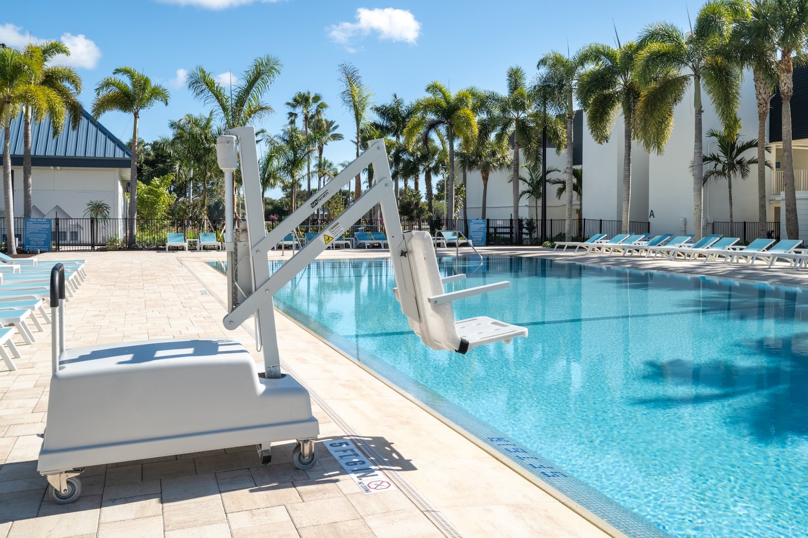Wheelchair lift at the edge of a clear blue pool surrounded by palm trees and white lounge chairs at voco Sandpiper All-Inclusive Resort.