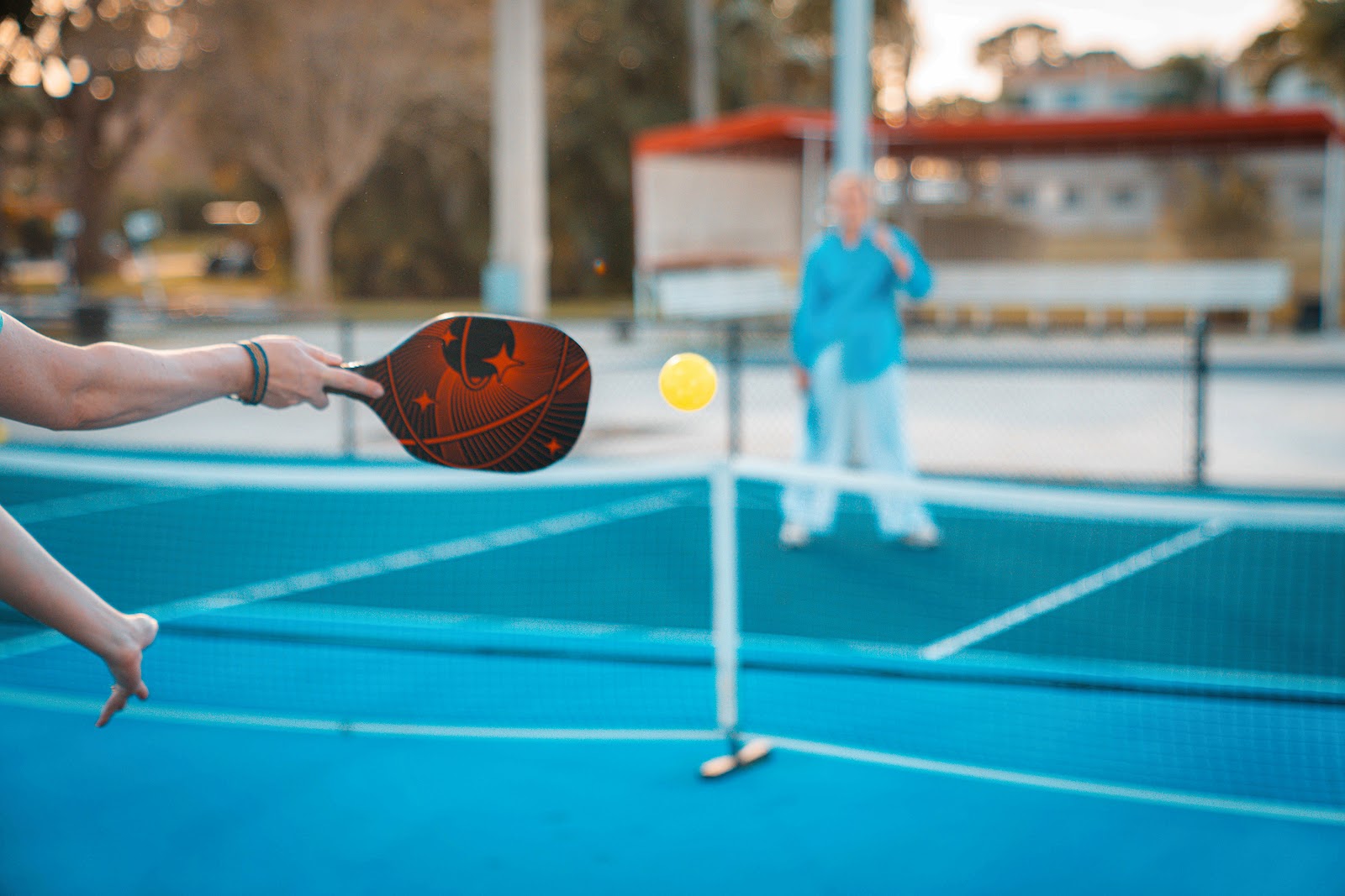A player holds a paddle mid-volley during a pickleball game on a bright blue court at voco Sandpiper All-Inclusive Resort, with another player in the background.