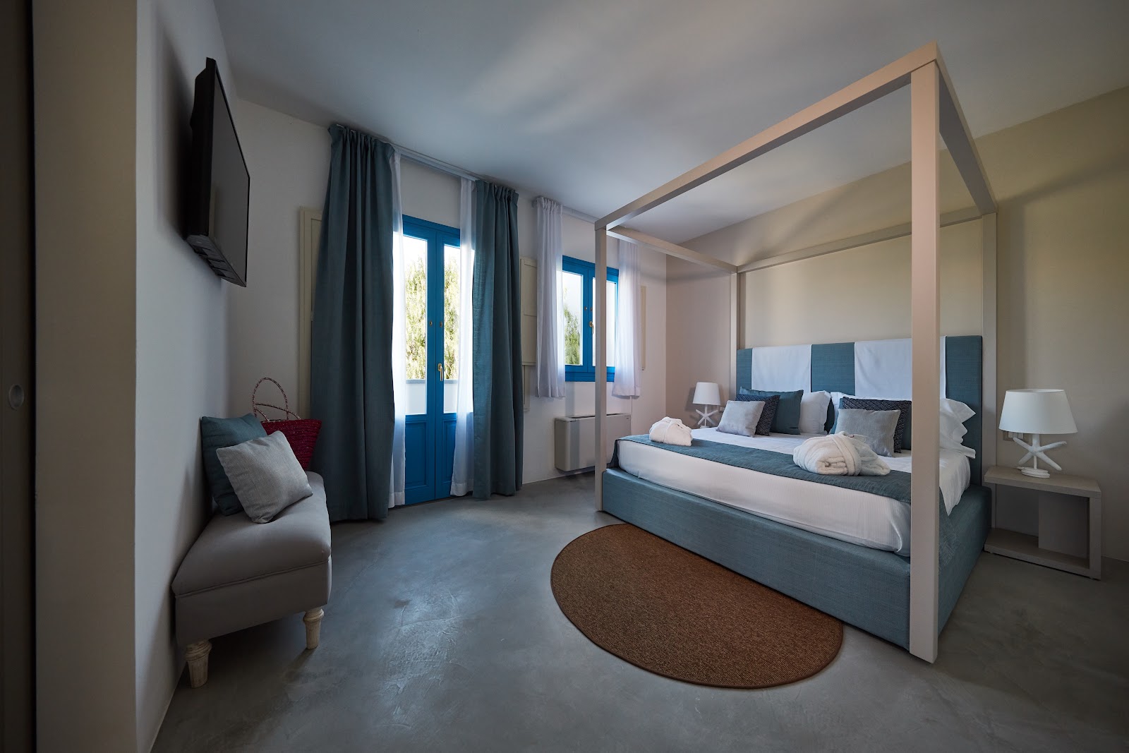 Resort bedroom with four-poster bed, blue accents, seating area, and blue doors opening to outdoor views.