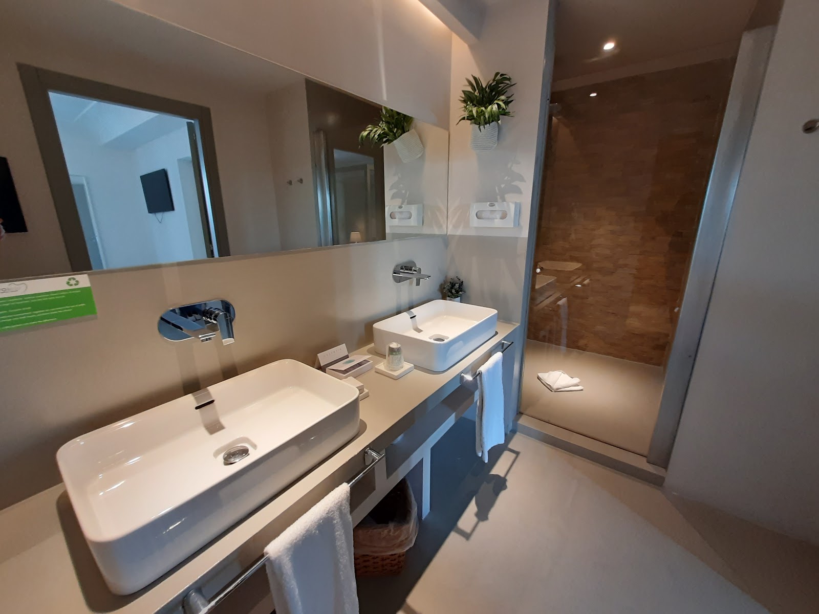 Modern bathroom with dual white sinks, large mirror, potted plants, and walk-in shower at VOI Marsa Siclà Essentia.
