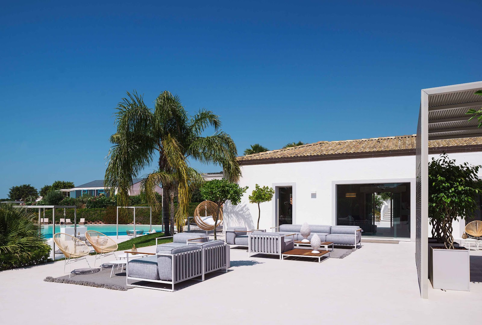 Oceanfront terrace at VOI Marsa Siclà Essentia with lounge seating, hanging chair, and pool view under clear blue sky.