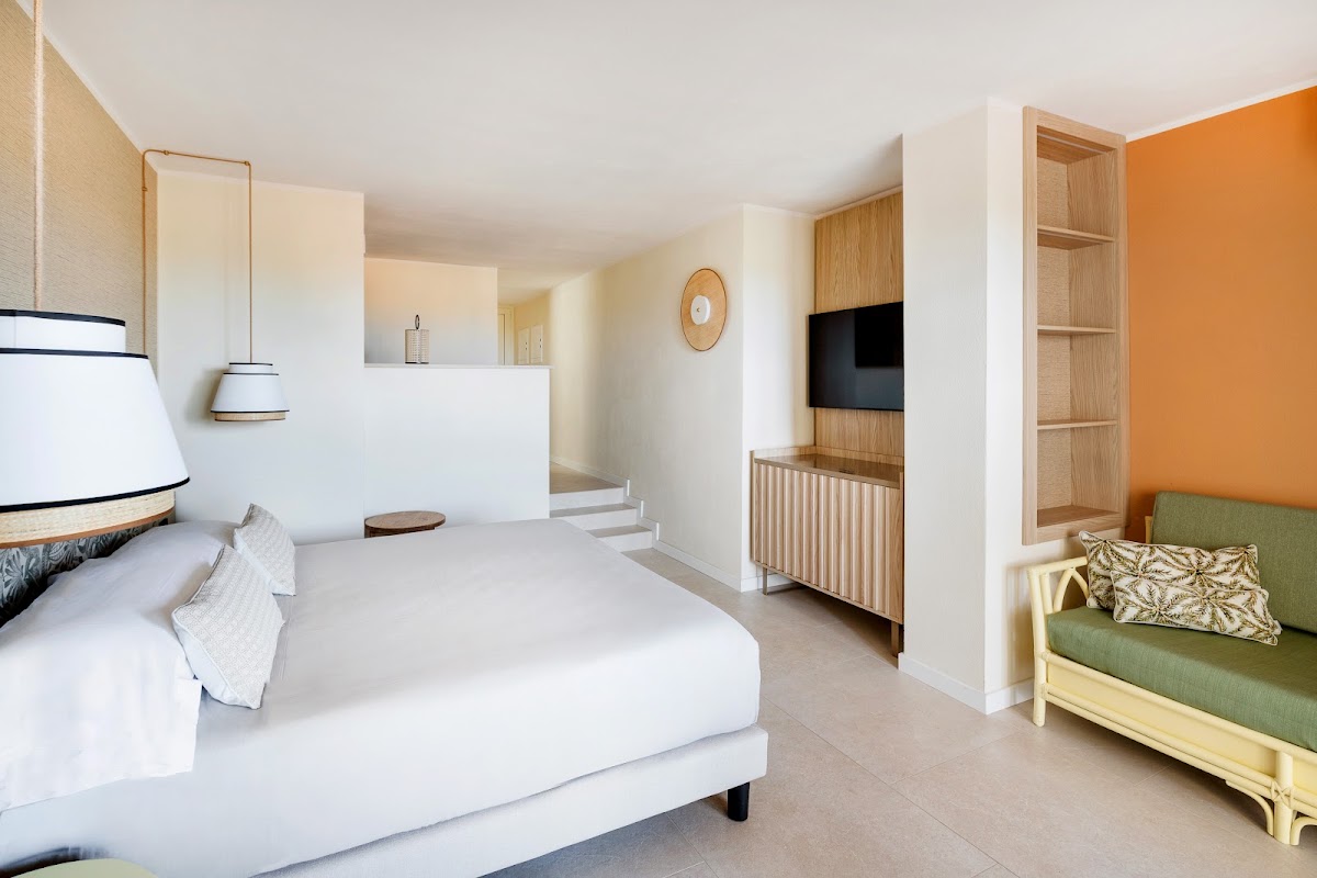 Spacious resort suite with white bed, orange accent wall, green sofa, TV, and wooden shelving at VOI Tanka Resort.