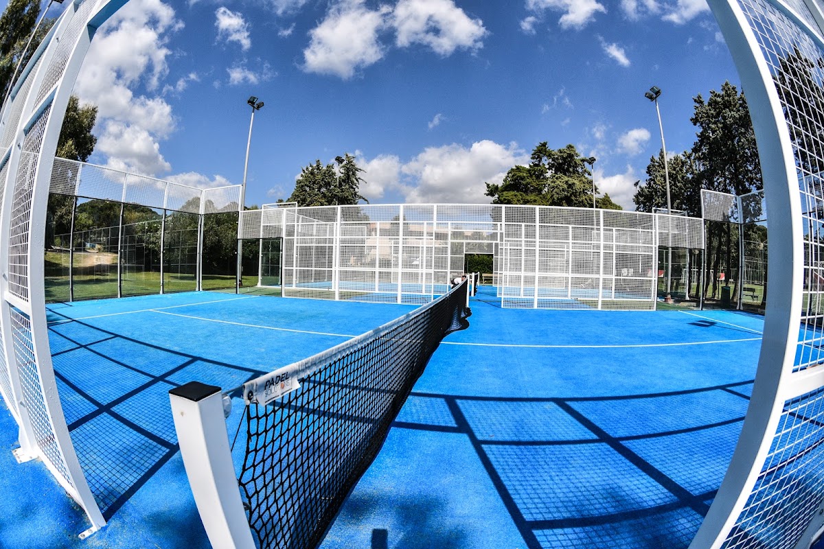 Multiple blue paddle tennis courts with white nets and fencing at VOI Tanka Resort, surrounded by tall trees and clear sky.