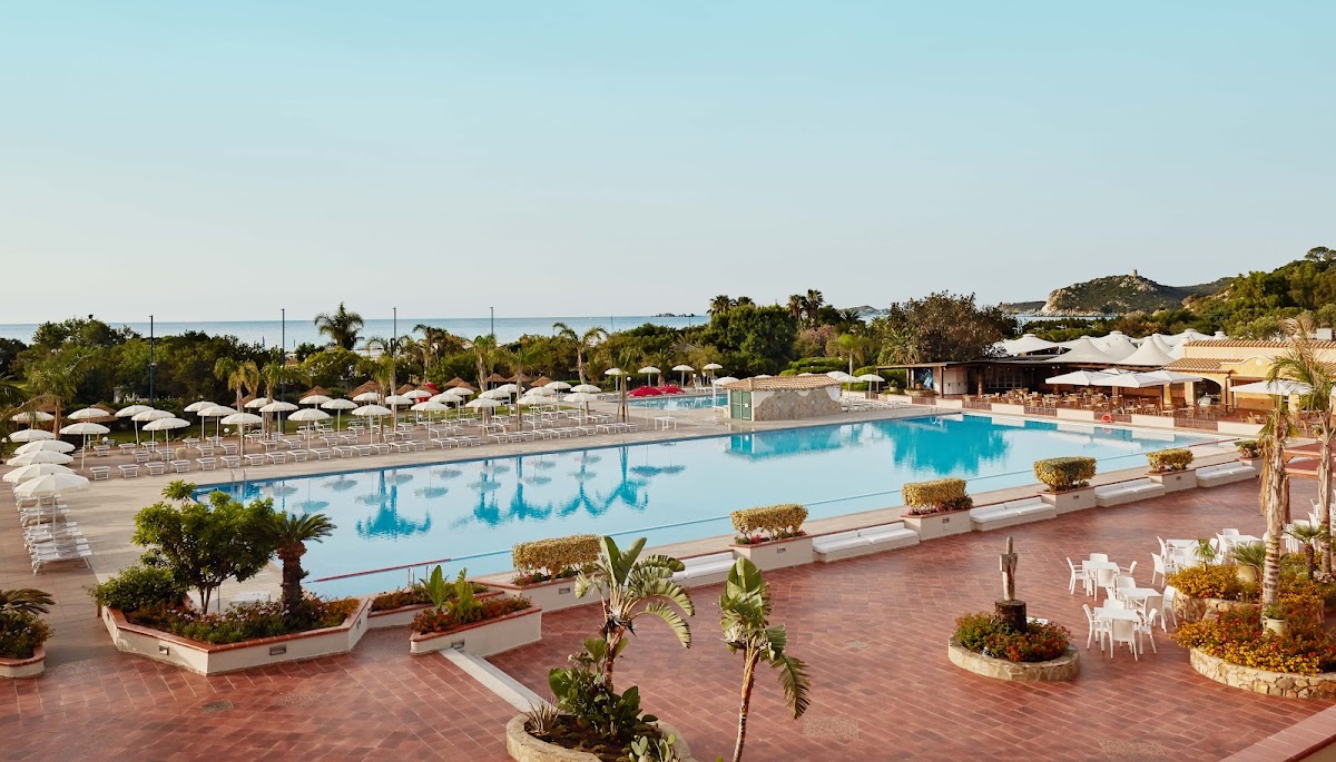 Large resort pool with terracotta deck, white umbrellas, loungers, and palm trees, with sea visible in distance at VOI Tanka Resort.