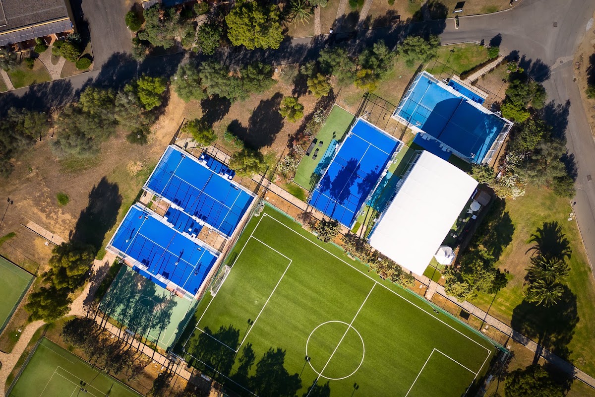 Aerial view of VOI Tanka Resort showing blue tennis courts, soccer fields, and a white tent surrounded by pine trees and sandy grounds.