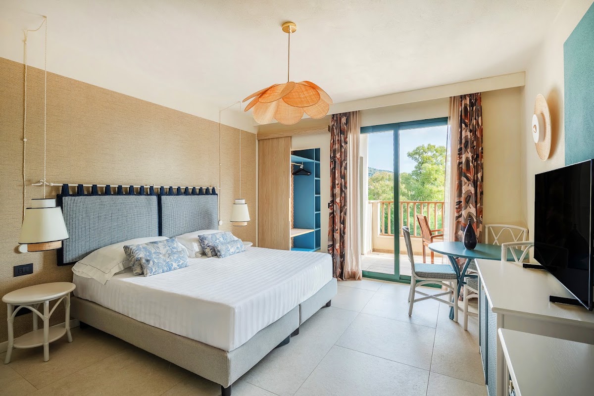 Resort guest room with king bed, orange pendant light, desk area, and balcony overlooking green landscape at VOI Tanka Resort.