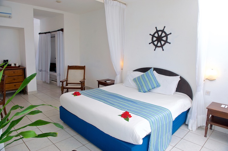 Spacious bedroom with blue bed, white linens, striped blue runner, ship's wheel wall decal, and nautical furnishings at Voyager Beach Resort.