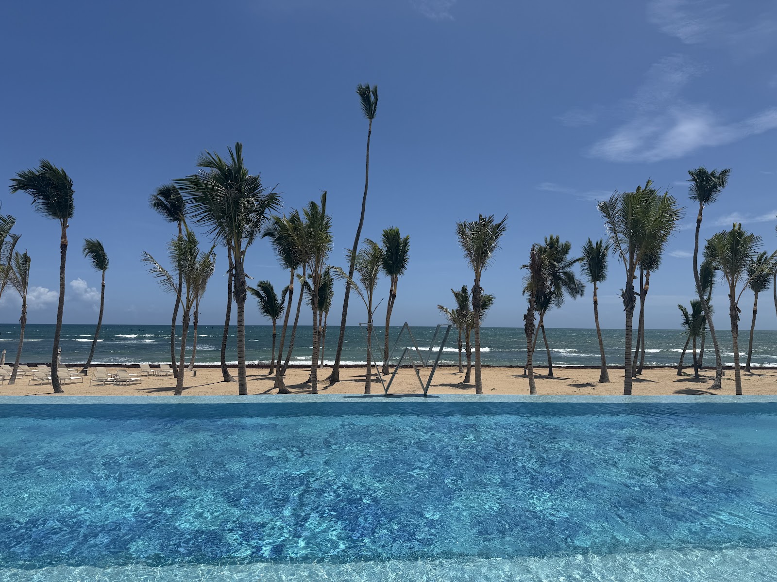 Clear turquoise pool with palm-lined beach and ocean beyond at W Punta Cana.