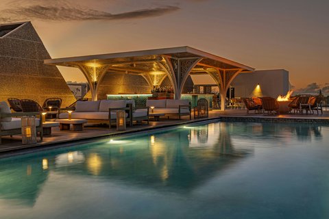Illuminated pool pavilion with lounge seating at dusk, W Punta Cana reflecting in calm water.