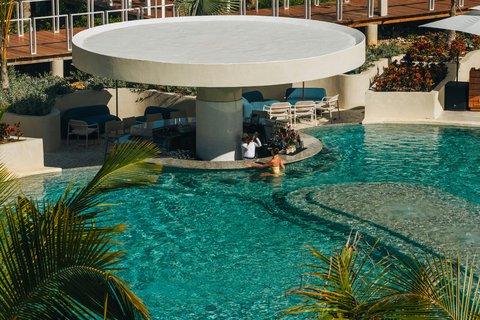 A guest swims in turquoise water near a circular poolside bar with blue seating and a white dome roof at W Punta Cana.