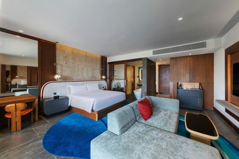 Modern suite with king bed, blue circular rug, gray seating area with red accent pillow, and wood accents throughout at W Punta Cana.