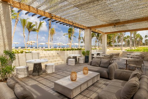Open-air lounge with gray seating, low tables, and ocean views through palm trees at W Punta Cana.