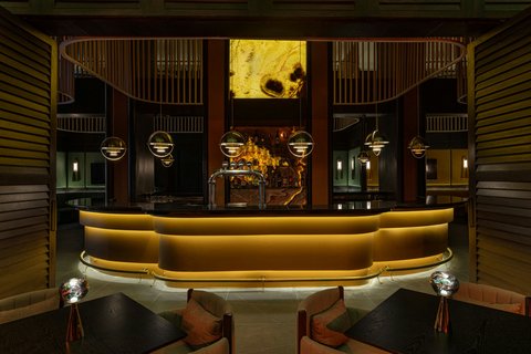 Curved gold reception desk in modern lobby with dark wood paneling, pendant lights, and glowing artwork overhead.