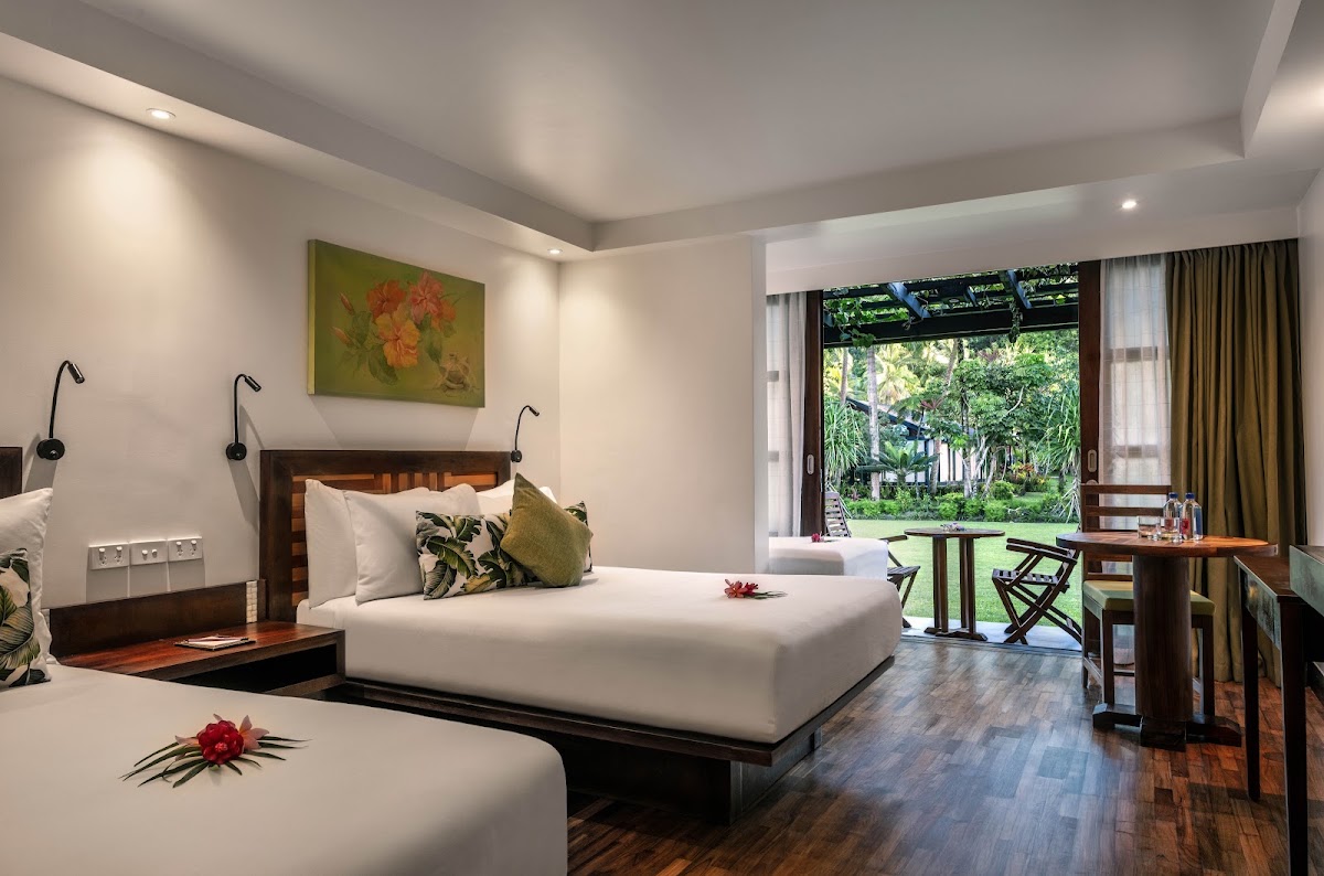 Spacious resort bedroom with two beds, tropical garden view through sliding doors, and wooden furnishings at Warwick Fiji.