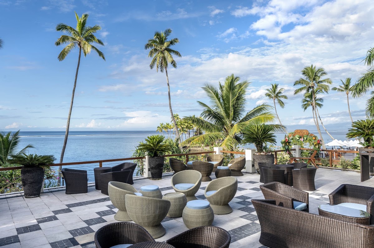 Oceanfront terrace at Warwick Fiji with woven seating, potted palms, and calm blue waters stretching to the horizon.