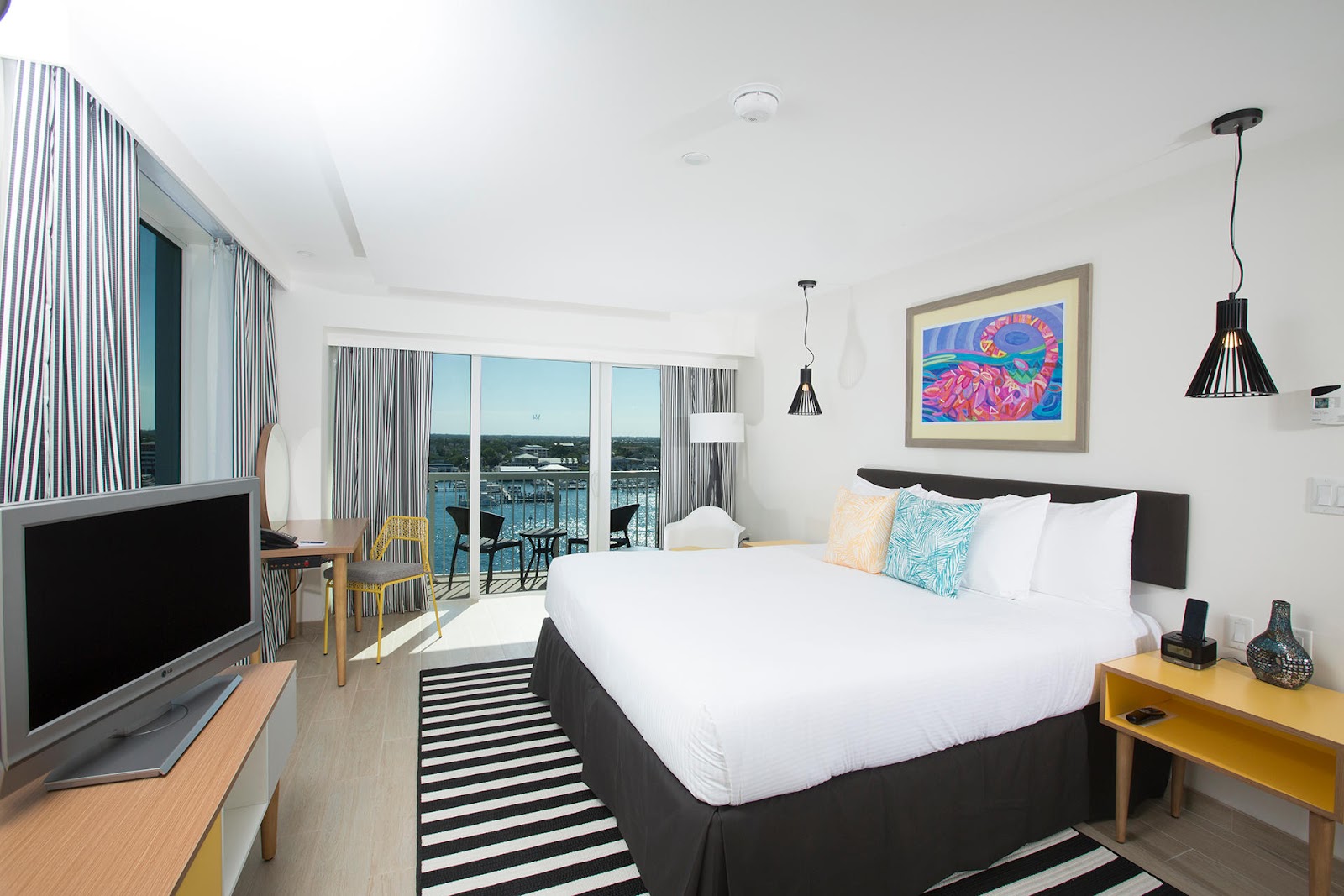 Modern resort bedroom with king bed, balcony overlooking marina and water, TV, and colorful artwork at Warwick Paradise Island Bahamas.