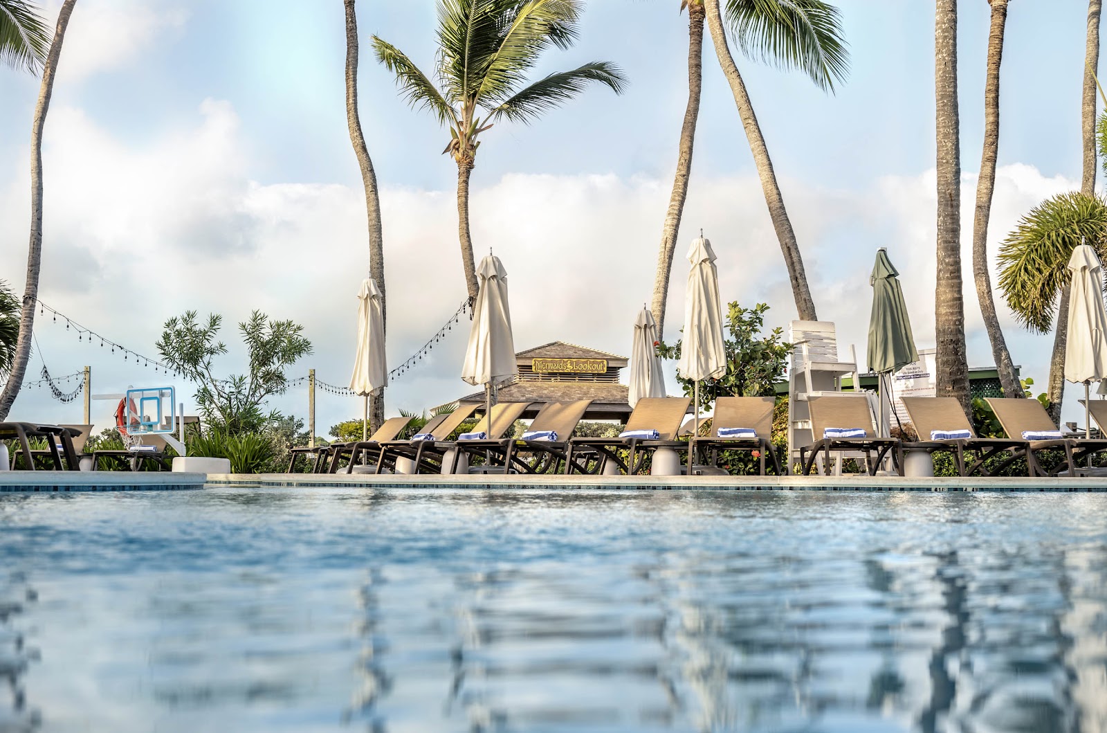 Pool view at Warwick Paradise Island Bahamas with lounge chairs, umbrellas, and tall palm trees under cloudy sky.