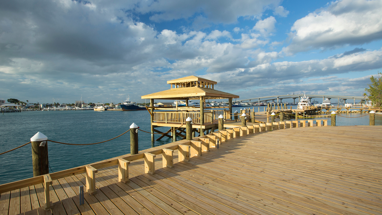Wooden pier with yellow gazebo extends into turquoise water at Warwick Paradise Island Bahamas, with boats and marina visible across the bay.