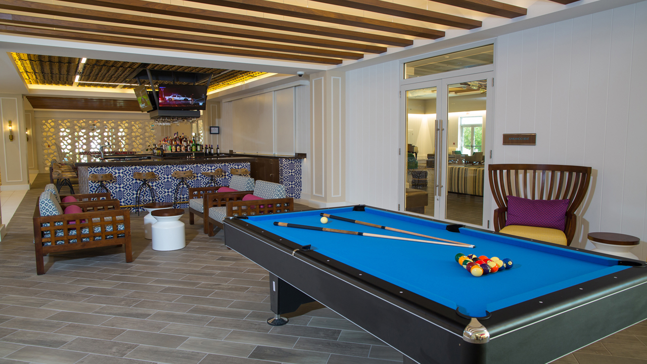 Recreation room with blue pool table, wooden furniture with pink cushions, patterned bar counter, and TV at Warwick Paradise Island Bahamas.