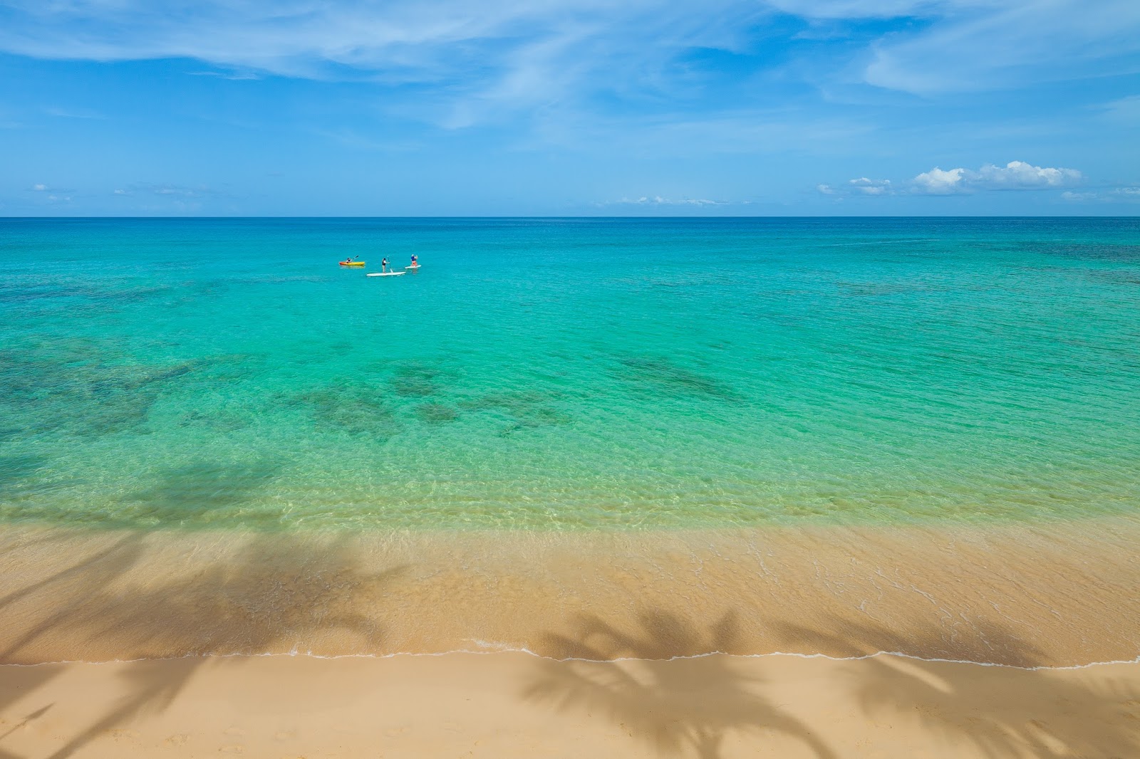Sandy beach with turquoise water and a small fishing boat offshore under blue sky at Waves Resort & Spa, Barbados.