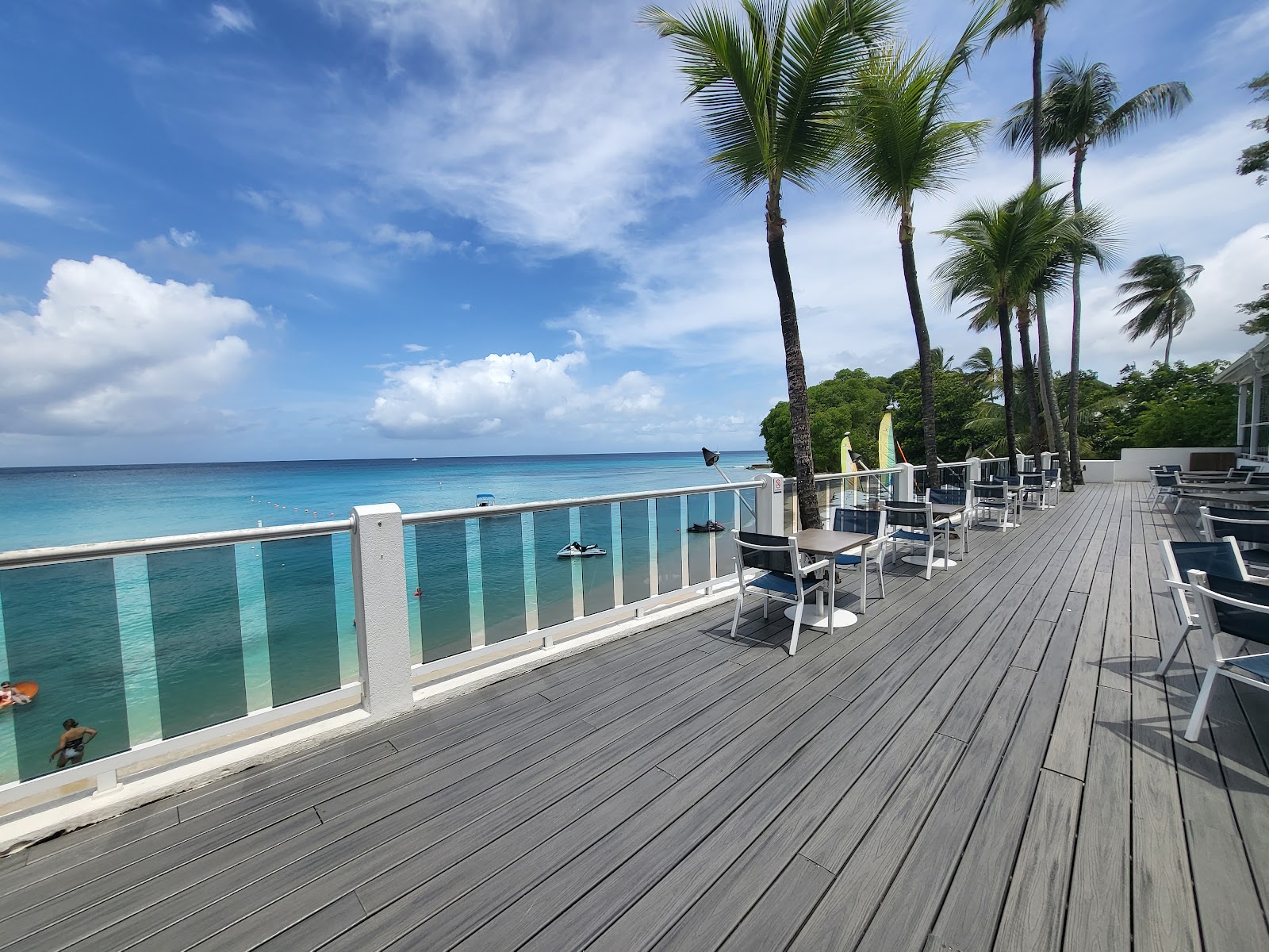 Wooden deck at Waves Resort & Spa overlooking turquoise Caribbean waters, with lounge chairs and tall palm trees lining the oceanfront.