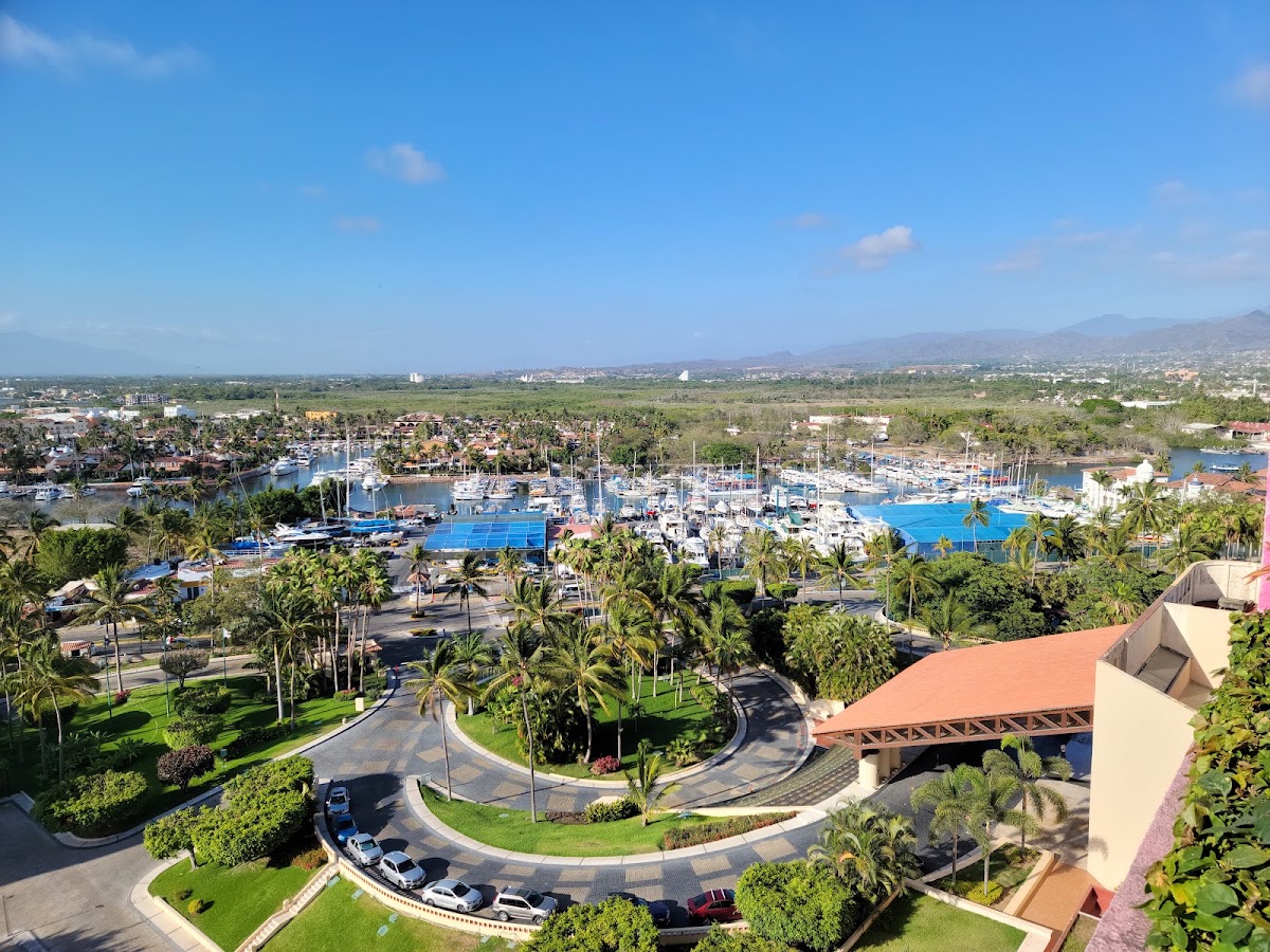 Aerial view of The Westin Playa Vallarta with manicured grounds, palm trees, blue pool complex, marina with boats, and valley landscape beyond.