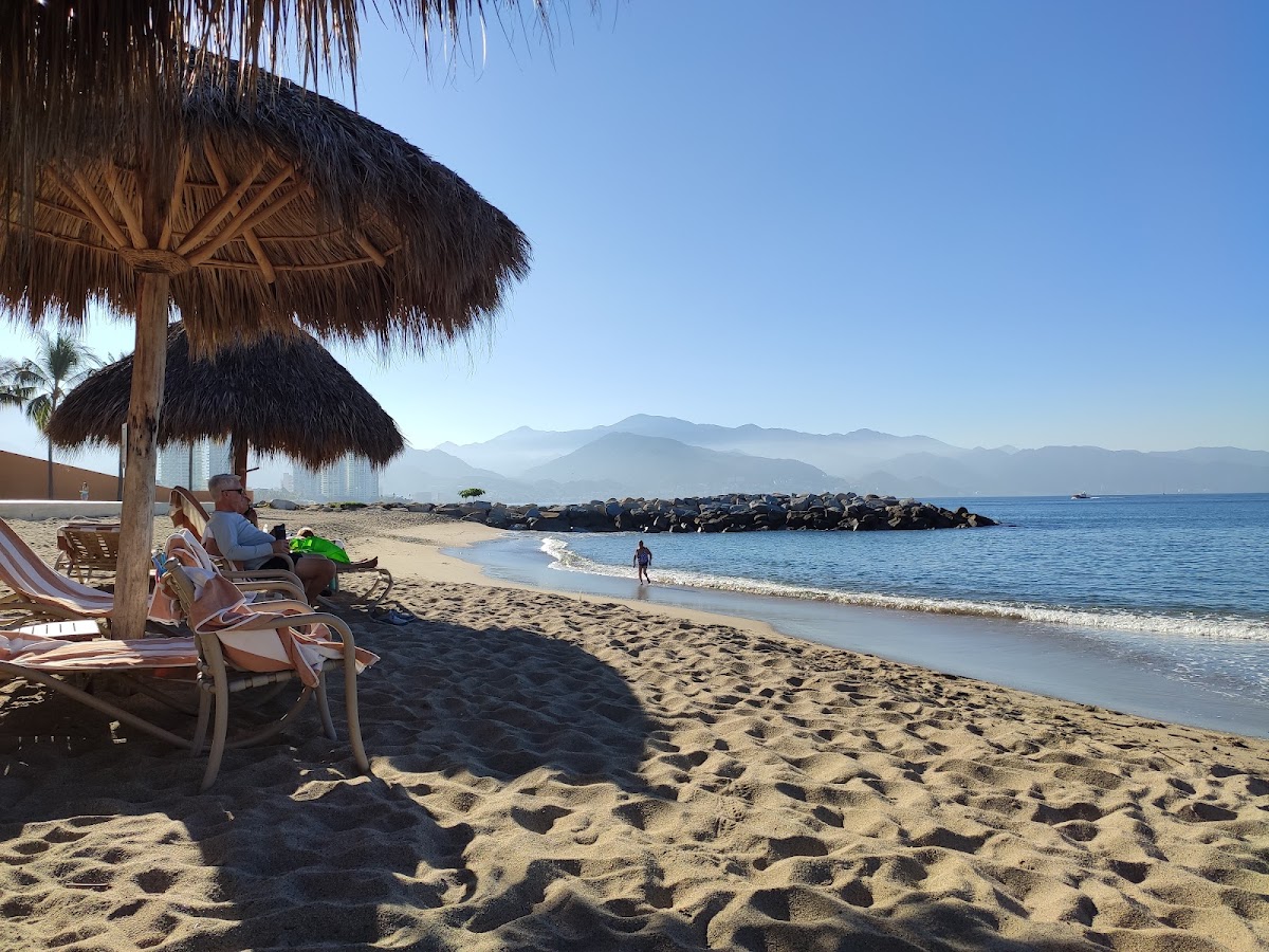 Guests relax under a thatched umbrella on the sandy beach at The Westin Playa Vallarta, with mountains visible across the water.