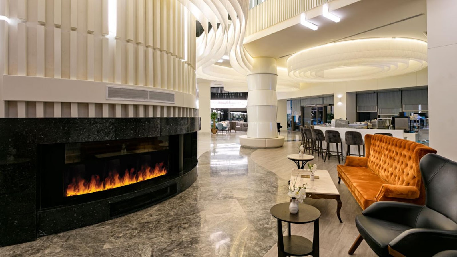 Modern lobby with electric fireplace, orange velvet sofa, bar seating, and curved ceiling details at Wind of Lara Hotel & Spa.
