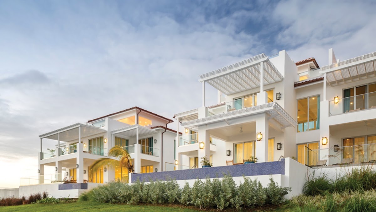 White stucco resort buildings with pergolas and balconies overlook manicured grounds and landscaping at dusk.