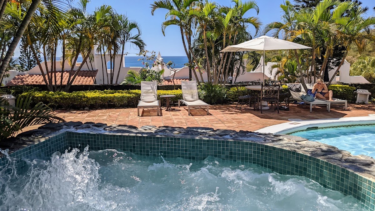 Whirlpool spa with bubbling water in foreground, lounge chairs and umbrellas on terra cotta patio, palm trees, and ocean view at Windjammer Landing.