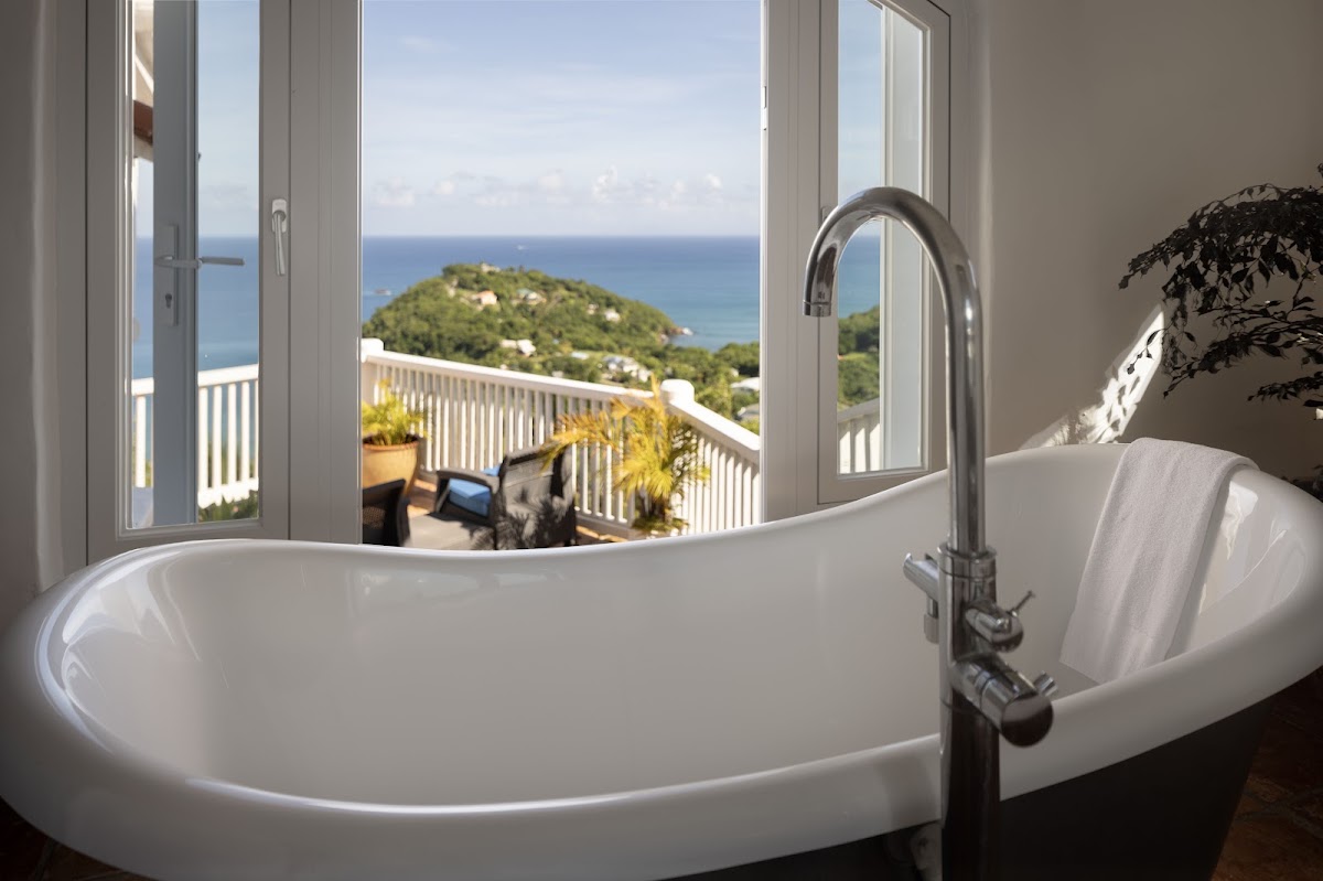 Freestanding bathtub with ocean view through open doors to a balcony overlooking a green island and turquoise Caribbean Sea at Windjammer Landing.