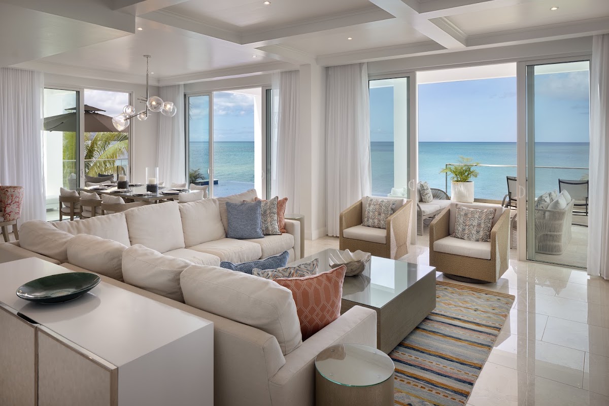 Beachfront suite at Windjammer Landing with cream sofa, ocean views through floor-to-ceiling windows, and turquoise Caribbean Sea beyond the terrace.