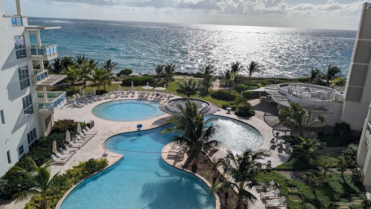 Aerial view of multiple pools, lounge chairs, and palm trees at a beachfront resort overlooking the ocean.